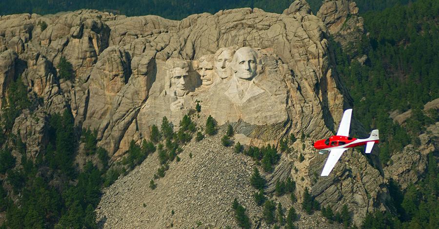 A Cirrus Airplane flying in front of Mount Rushmore